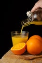 View of woman`s hand serving orange juice from a bottle, on wooden table with oranges, in portrait, Royalty Free Stock Photo