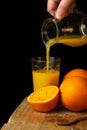 View of woman`s hand serving orange juice from a jug, into a glass, on wooden table with oranges, in portrait, Royalty Free Stock Photo