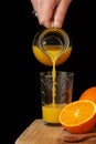 View of woman`s hand serving orange juice from a jug, on wooden table with half orange Royalty Free Stock Photo