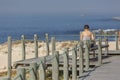 View of woman seat on wood bench in pedestrian wooden walkway, beach and sea as background