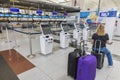 View of woman sitting on carry-on bag in front of baggage drop-off sign in airport. New York.