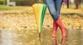 A view of a womans legs in rubber boots standing in a puddle, leaning on an umbrella. A woman standing in a puddle surrounded by