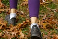 view of a women`s feet as she walks over grass covered with fallen leaves of red maple tree.