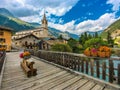 Wooden bridge over alpine river and houses with church in Val-Cenis, France Royalty Free Stock Photo