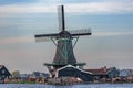 View of a working windmill in the middle of an old Zaans village on a river. background a striped blue and white sky.