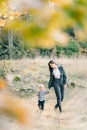 View through the yellow leaves on the mother with a little girl walking on a green meadow