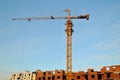 View of a yellow tower crane and a brick residential building under construction against a blue sky in the early morning. Royalty Free Stock Photo