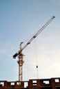 View of a yellow tower crane and a brick residential building under construction against a blue sky in the early morning. Royalty Free Stock Photo