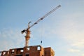 View of a yellow tower crane and a brick residential building under construction against a blue sky in the early morning. Royalty Free Stock Photo