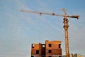 View of a yellow tower crane and a brick residential building under construction against a blue sky in the early morning. Royalty Free Stock Photo