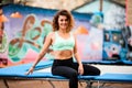View on woman with curly hair in bright sports top sitting on trampoline