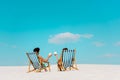 View of young couple sitting in deck chairs with coconut drinks on sandy beach Royalty Free Stock Photo