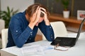 Young man holding his head in a desperation gesture while looking at some bills on a table next to a laptop. Payment and Royalty Free Stock Photo