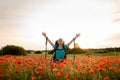 View on young smiling woman with backpack who stands on poppy field with hands up Royalty Free Stock Photo