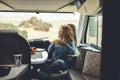 View of young woman sitting and having leisure time inside a camper van motor home. Independent lifestyle female