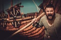 Viking with axe standing near drakkar on the seashore.