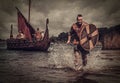 Viking warrior in the attack, running along the shore with Drakkar on the background.