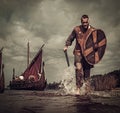 Viking warrior in the attack, running along the shore with Drakkar on the background. Royalty Free Stock Photo