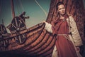 Viking woman standing near Drakkar on the seashore.