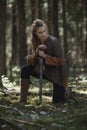 Viking woman with sword wearing traditional warrior clothes in a deep mysterious forest.