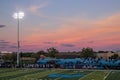 High School football game with night lights on and sun setting in sky Royalty Free Stock Photo