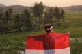 a village boy unfurls a red and white flag with both hands in a rice field, sunset background.