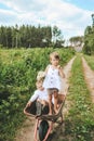 Village children play with a garden wheelbarrow. Little girl threatens with a fist to fight