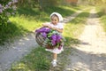 A village girl in a white dress and a kerchief carries a basket filled with spring blooming flowers and violet lilac along a count Royalty Free Stock Photo