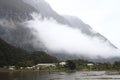 Village with green vegetation and mountains covered in clouds. Milford Sound, New Zealand. Royalty Free Stock Photo