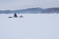 The snowmobile with fishermen is riding along the winter lake.