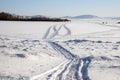 Trace from snowmobile on a snowy lake with fishermen in the background