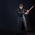 A villain with a red lightsaber, a young man in a long robe does fighting poses,