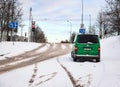 Vilnius, Lithuania- December 26 2021: Green car standing on snowy road with road signs, trees and wires on blue sky
