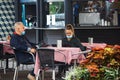 Vilnius, Lithuania - 30082020: Man and woman sitting in street cafe wearing facial masks reading manu waiting to order