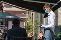 Waiter with a mask serving client at the table