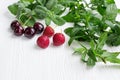 Cherries, strawberries, fresh mint and melissa herbs on white wood