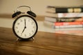 Vintage alarm clock on rustic wood table. Shows 7 o'clock. Pile