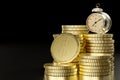 Vintage alarm table clock on a stack of coins in dark black background.