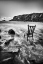 Vintage antique chair tucked into the water of an Irish beach surrounded by rocks and cliffs. long exposure with traces of water. Royalty Free Stock Photo