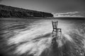 Vintage antique chair tucked into the water of an Irish beach surrounded by rocks and cliffs. long exposure with traces of water. Royalty Free Stock Photo