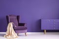 Vintage armchair, beige blanket and cabinet set on a violet wall