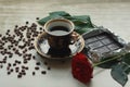 Vintage beautiful cup of hot coffee, bright red rose, green leaves, scattered coffee beans and dark chocolate bar on a wooden tabl Royalty Free Stock Photo