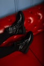 Vintage black leather brutal women`s boots with lacing close-up on a red sofa in the store. Modern young woman in stylish autumn