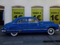 Vintage blue car parked in front of signs with the text in Spanish `todo a 1 euro` everything at 1 euro