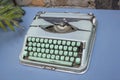 Vintage blue typewriter with turquoise green buttons stands on a table with a branch of a plant