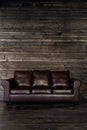 Vintage brown leather sofa on a wooden wall and floor Royalty Free Stock Photo