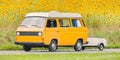 Vintage camper bus with popup camper driving alongside a field with sunflowers