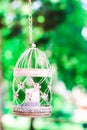 Vintage candle in decorative bird cage. White birdcage on floral background. Wedding decoration, green foliage and lantern.