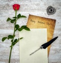 Vintage card with red rose, white book, ink and quill on white painted oak - top view