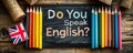 Vintage chalkboard with Do You Speak English? question, British flag, and pencils on rustic wooden backdrop, representing Royalty Free Stock Photo